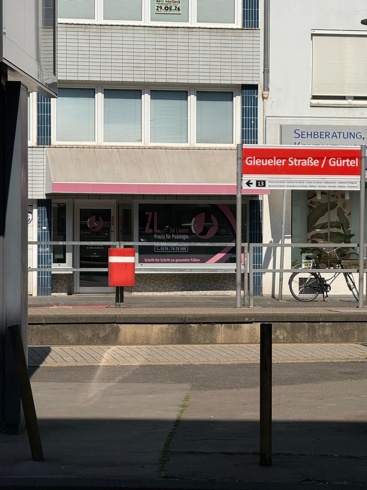 Rotes Stationsschild Gleueler Strasse Guertel vor grauem Gebaeude und Rad